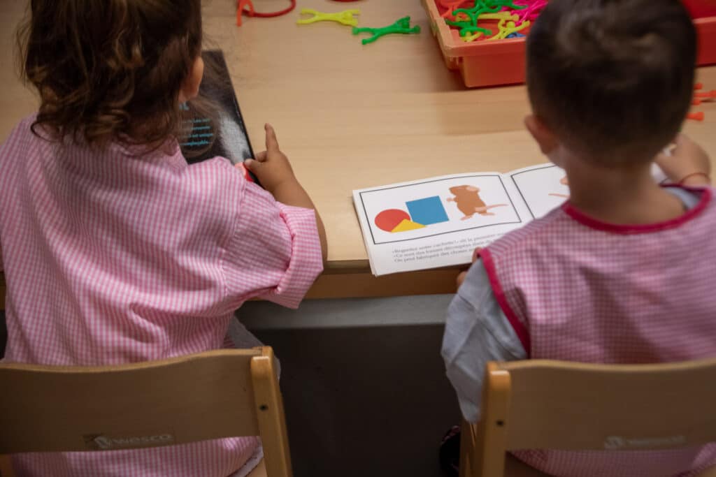 Deux enfants de maternelle découvrent les couleurs à travers un livre illustré, lors d’une activité de lecture en classe accompagné du personnel.